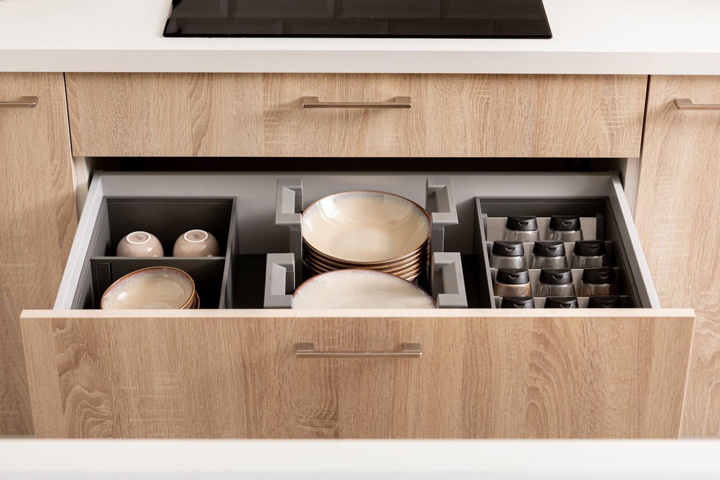 Kitchen drawer containing dishes, cups and spices in divided sections.