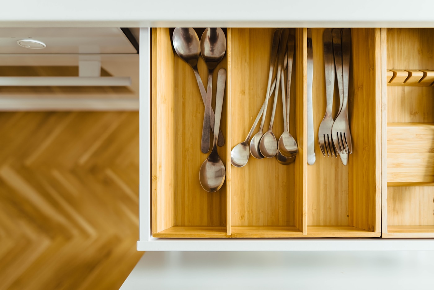 Open wooden kitchen drawer with cutlery in separate compartments.